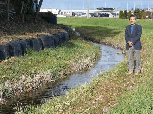 山下川の親水活動に取り組む三石猛さん。背後にＬＲＴの車両が見える