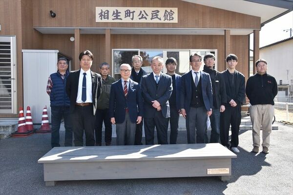 寄贈された木造ベンチと三ツ山委員長（前列左から２人目）と安達理事長（同３人目）ら