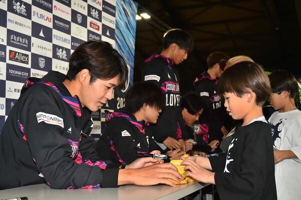 子どもの靴にサインする栃木シティのＦＷ吉田（左）＝日環アリーナ栃木
