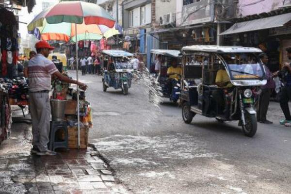 27日、インド・ニューデリーで路上に水をまく男性(共同)