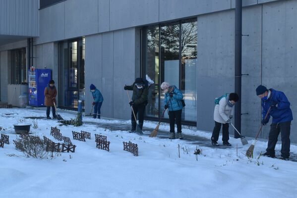 クリスマスローズがなくなった花壇周辺を雪かきするグループのメンバー。「これからも花を植えてきれいにしたい」との声も＝１月30日、仙台市青葉区