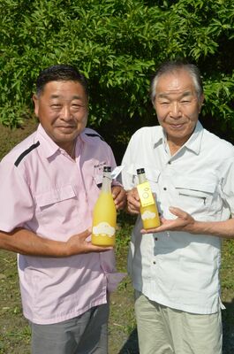 リキュールを持つ種無しユズ生産者の石河さん（右）と、製品化した村上社長