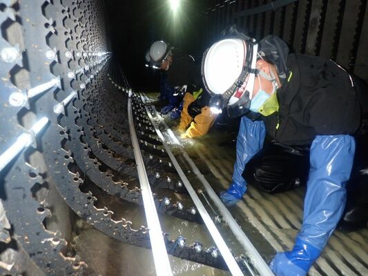 汚水が流れる中、鋼製リングに表面部材を組み付ける作業員（宇都宮市上下水道局提供）
