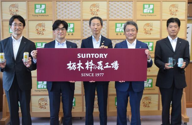 新たな工場名が書かれたプレートを掲げる岡専務執行役員（右から２人目）と天利副知事（中央）＝21日午後、県庁