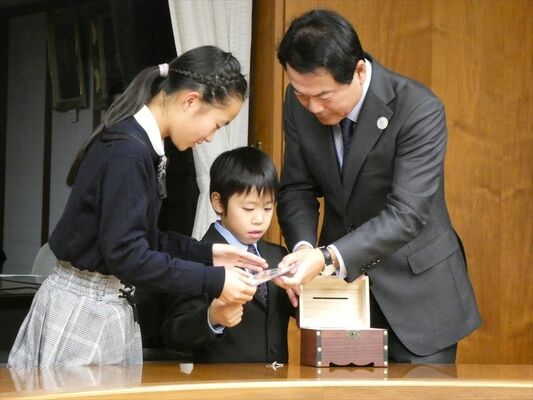 宝箱形のタイムカプセルにＤＶＤを詰める佐藤市長と石川さん（左）、皿井君（中央）