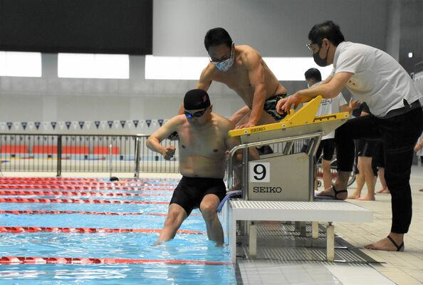 水泳の強化練習会で指導者らに支えられて入水する選手＝９日、宇都宮市西川田４丁目