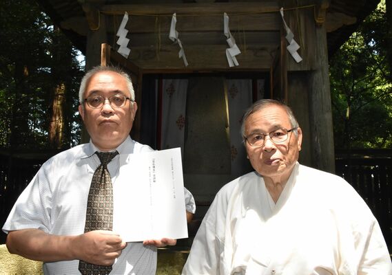 笠石神社の国造碑の前で冊子を持つ大沼さん（左）