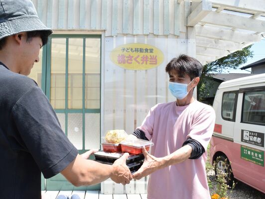新たにオープンした拠点施設で弁当を手渡す城田さん（右）