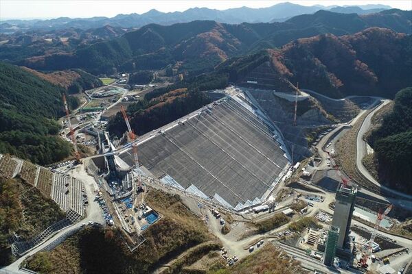 堤体の上流面（右）で表面遮水壁のコンクリート打設が進む南摩ダム＝29日午後０時35分、鹿沼市上南摩町、ドローンから