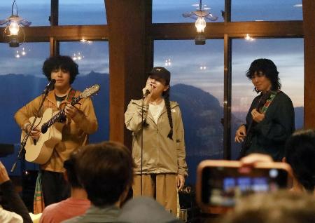 　夕焼けに染まった雲海を背にライブで熱演する「スーパー登山部」のＨｉｎａさん（中央）らメンバー＝２０２５年８月、北アルプス白馬岳山頂付近の白馬山荘