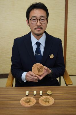 ヒノキ端材で試作した「ともなりくん」グッズのコースターを手にする室井さん