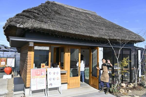 かやぶき屋根がシンボルマークの店先に立つ吉村さん