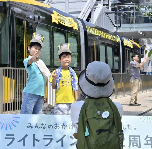 利用者1千万人達成を記念したラッピング車両の前で記念撮影する親子連れ=23日午前10時40分、宇都宮市宮みらい