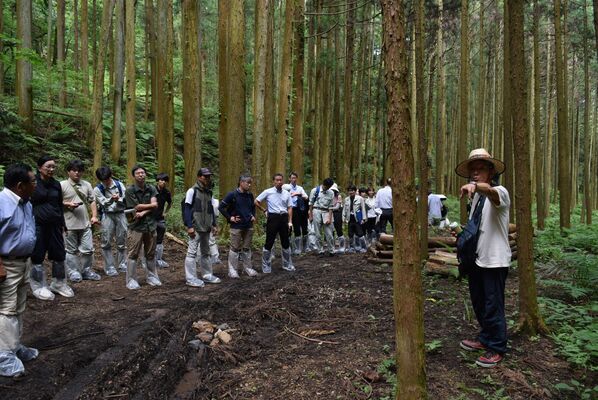 田中代表（右）から整備した里山の説明を受ける参加者＝８日午後、佐野市