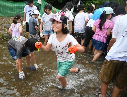 両手にニジマスをつかみ笑顔を見せる児童ら