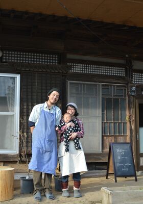 古民家の自宅に民泊とパンの店の看板を掲げた君島さん夫婦と、集落に27年ぶりに生まれた赤ちゃんの琉生ちゃん