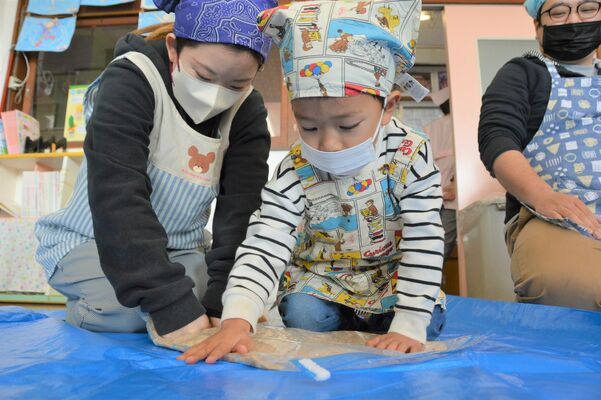 袋に入れた大豆を念入りにつぶす親子