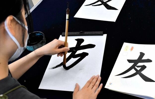 左手で筆を持つ場合、半紙を少し斜めに、筆置きは左、手本は右に置く工夫があると書きやすい＝７月末、松山市文京町の愛媛大
