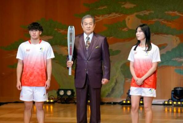 愛知・名古屋アジア大会の開幕まで100日となり、セレモニーで聖火リレーのユニホーム(左右)とともにトーチを披露する松平健さん=11日午前、名古屋市