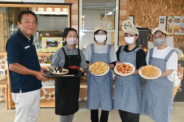 園内のレストハウスで販売しているピザとおにぎりを持つ相良さん（左）と従業員ら