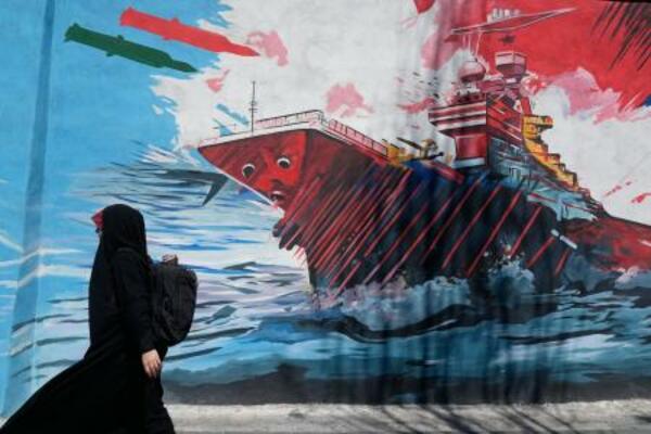イラン・テヘランでミサイル攻撃を受ける米空母を描いた壁画の前を通り過ぎる女性=8日(AP=共同)