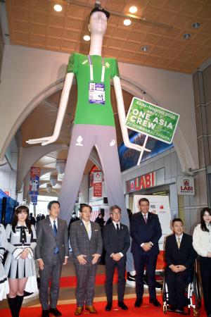 　愛知・名古屋アジアパラ大会でボランティアが着用するユニホームの特別サイズを着た「ナナちゃん」と記念写真に納まる関係者＝２８日午後、名古屋市