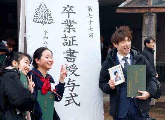 　長男泰介さんの写真と卒業証書を手に、泰介さんの友人らと記念写真に納まる大間圭介さん＝１３日午後、金沢市