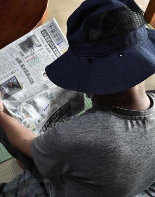 クマによる被害を報じる新聞に目を通す男性。負傷した頭には帽子をかぶっている＝４日午前、那須塩原市