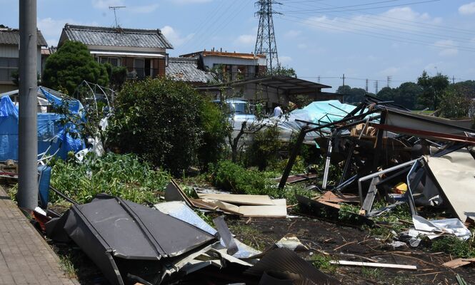 屋根が飛ばされた民家（奥側）。畑にはがれきが散乱している＝11日午前11時25分ごろ、野木町友沼