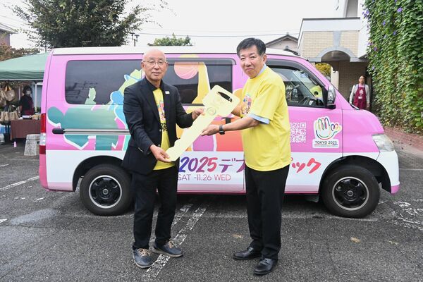 キャラバンカーの前で早川理事長（左）から鍵を受け取る稲川理事長＝４日午後、足利市助戸仲町