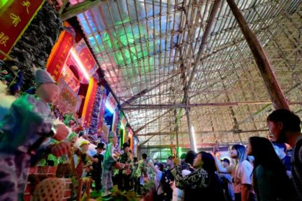 竹で造られた建物の中で、祭りの展示にカメラを向ける人々=18日、香港・新界地区元朗(共同)