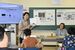 小金井空襲体験者の簗さん（右奥）から話を聞いた後、副読本に掲載された小金井空襲のページを示しながら児童に語りかける稲見教諭＝１３日午前、下野市細谷小
