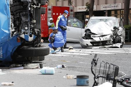 　2019年４月、東京・池袋の暴走事故で乗用車（奥）を調べる警察官。加速しながら自転車や通行人を次々はねるなどし、時速約96キロに達した