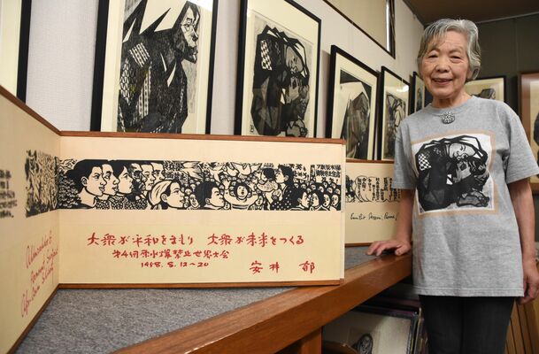 鈴木賢二の版画絵巻「平和を世界に」の横で平和への思いを語る四女解子さん