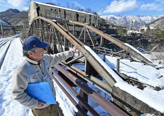 「銅山といっても身近に感じない人も多い。史跡だからこそ興味を持ってくれる人もいる」と話す山田さん。目の前のトラス橋は国重要文化財の古河橋＝２月中旬、日光市足尾町赤倉