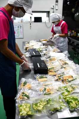 栄養バランスを考えたおかずを１食分ずつ真空パックに詰めるスタッフ＝７月中旬、宇都宮市