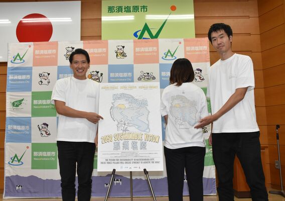「２０５０　サステナブルビジョン」のポスターとＴシャツを紹介する渡辺市長（左）ら