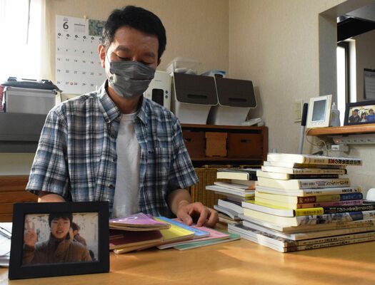 民事裁判の記録などを書き記したノートを手にする奥さん。手前の写真は息子の公輝さん＝25日午後、さくら市氏家
