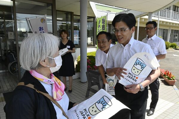 来庁者に牛乳のPRグッズを手渡す神林町長(右手前)ら