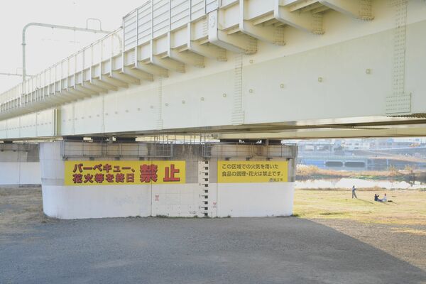 東京都狛江市がバーベキューなどを禁止している多摩川緑地公園グラウンド。小田急小田原線の橋脚に禁止を知らせる大きな案内板が設置されている