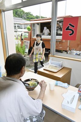 目の前で調理されたラーメンを食べる利用者ら