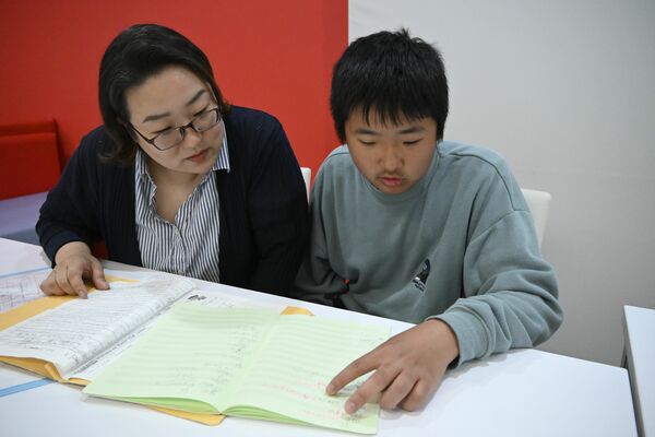 学習障害に加えて感覚過敏があり、ミント色のノートで勉強している大澤さん（右）と母＝12日午後、真岡市内