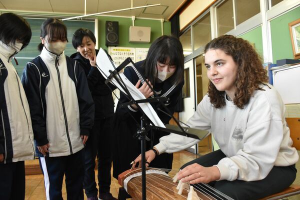 合唱交流会後、三島中を訪れたオーストリアの学生と琴の演奏を楽しむ生徒たち＝３月