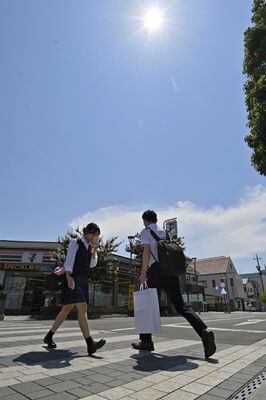 強い日差しが降り注ぐ中、小型扇風機などで暑さをしのぐ通行人たち＝22日午後１時20分、佐野市若松町