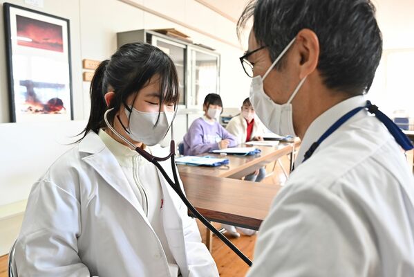 小児科医（右）のアドバイスを受けながら聴診器で心音を聞く生徒