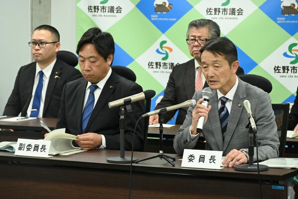 可決後の記者会見で報告書について説明する菅原委員長（右）＝12日午後５時５分、佐野市役所