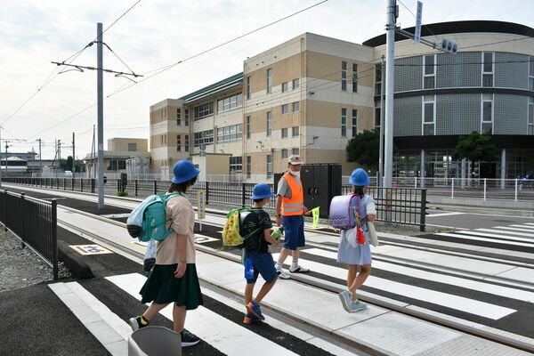 交通指導員に誘導されて軌道敷を横断する児童たち＝７月18日、午前７時40分、宇都宮市下平出町