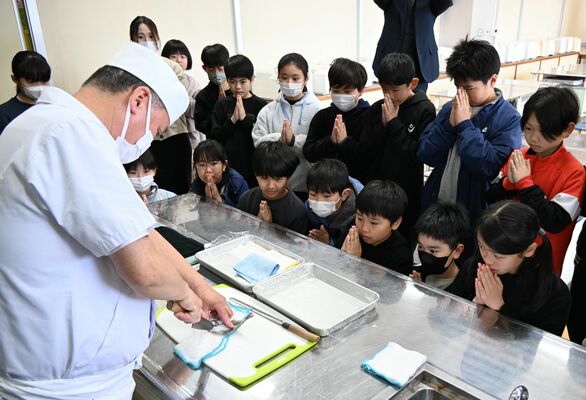 ヒラメをさばく様子を手を合わせて見守る児童たち