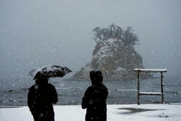 雪が降りしきる中、石川県珠洲市の景勝地「見附島」を訪れた人たち。能登半島地震の発生から2年となった=1日午前7時5分