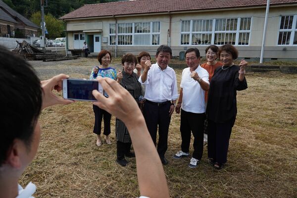母校の分校跡で同級生らと記念撮影する茂木氏（右から４人目）ら＝11日午後、足利市月谷町